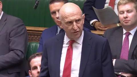 John Healey stands in the House of Commons