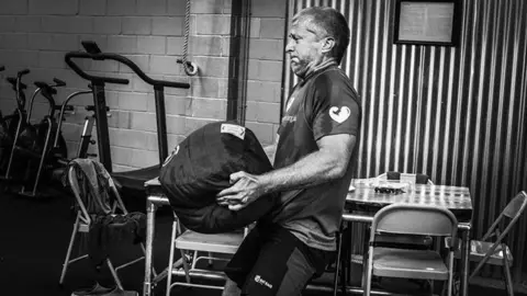 Efrem Brynin A man trains at a gym holding a heavy object 