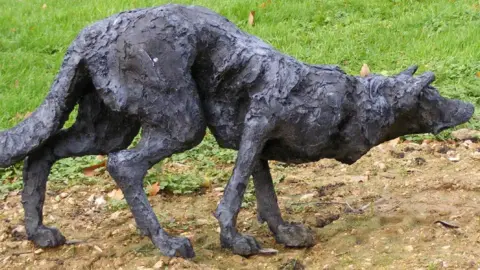 Side view of the stalking dog sculpture. The black cast sculpture resembles a border collie when it stalks sheep. Its head is low, tail is down and ears are forward.