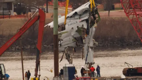 Crews use a crane to lift plane wreckage out of a river.