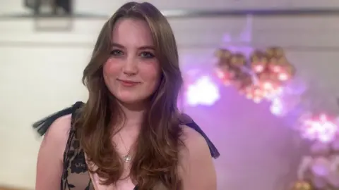 Mousumi Bakshi/BBC Sophie Carey wearing a nude and black lace prom dress in Harlow