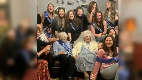 Family handout Close up of an elderly woman dressed up for her hen do with a veil. She is sat with other women who have funky glasses on.