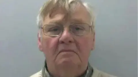 Police mugshot of former Sunday School teacher John Laister, wearing a green shirt, white jumper and glasses. He is already serving a sentence for raping and sexually abusing young girls under his care in West Yorkshire