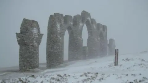 Simon Richardson/Geograph The monument, built to resemble the ruined gates of Negatapam, a town in India, is pictured in a snow storm. The sky is grey and snow covers the ground.