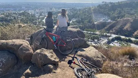 Dua pengendara sepeda duduk di samping sepeda mereka di sebuah bukit yang menghadap LA