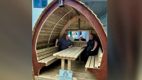 A triangular wooden seating pod with two men sitting in it