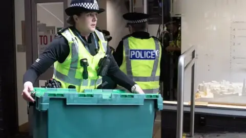 PA Media Police woman holds box outside an office