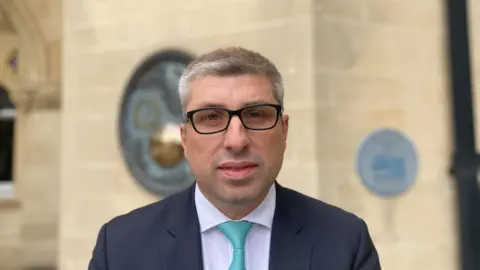 Mark Arnull standing in front of the Guildhall wearing a suit with a light blue tie