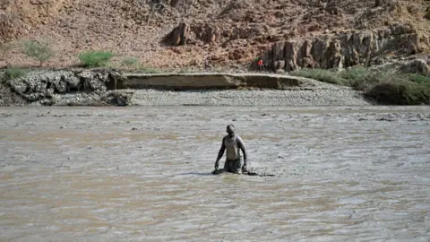 AFP An image of a person wading through the muddy waters of the dam collapse