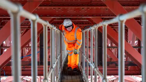 Man in orange hi-vis and white hard hat, underneath the railway line on the Forth Bridge