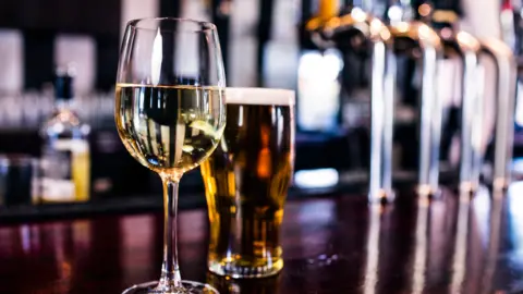 Glass of wine and pint of beer placed beside pumps in a pub