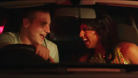 Signature Entertainment Luke (played by Ben Hardy) and Aysha (played by Jason Patel) laughing together in a car