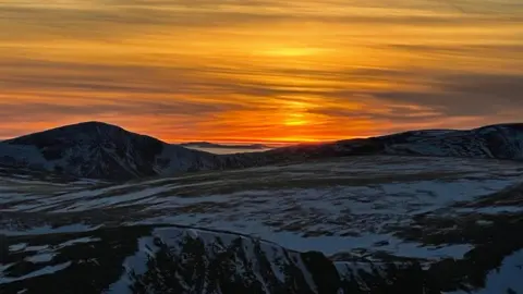Caroline Drummond A sunset over a snowy mountain, with the sky lit up orange