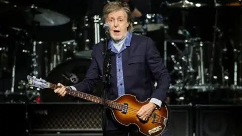 Sir Paul performs during his Got Back tour in London in December 2024 - he's in a blue suit and shirt playing the guitar on stage 