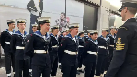 Jersey Sea Cadets A group of young sea cadets stand at attention in uniform in front of a commanding officer