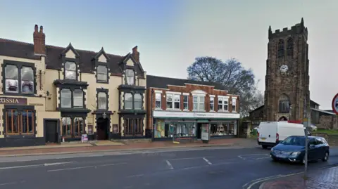 Google Streetview image of Heanor Market Place, showing a row of shops in traditional buildings and a church