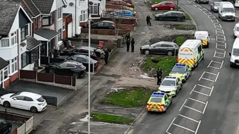 A drone image of police vehicles parked in Broad Avenue in Leicester and a number of officers around a property in the street 