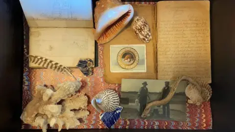 Julia McKenzie Art made by Julia McKenzie with the diaries she found from her father. It includes old photos, some sea shells and a feather.