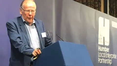 Humber LEP A man with glasses and wearing a blue suit stands at a lectern delivering a speech.