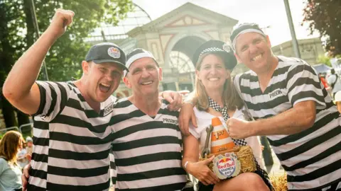 Red Bull Paul Beesley, Lee Masser and Jon Chaproniere wearing black and white-striped prisoner outfits, with Jo Chaproniere dressed as a police officer. They are celebrating their win.