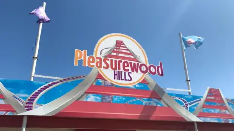 The main bright pink and blue sign reading Pleasurewood hills, flanked on both sides with flags 