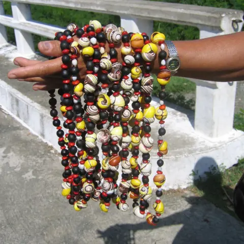Angus Davison hand the man's hand, the rest of which came out of the shot, withstand about 10 colorful, beading necklaces thrown over him. If you look more closely, some of these beads are actually colorful shells. Some of them are the disappearing shells of polymite. 