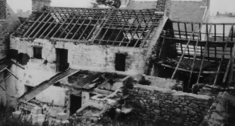 Alderney Museum A black and white image of a birds eye view of a destroyed home in Alderney from 1945. There is no windows, roof or doors. 