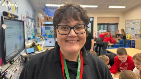 Phillip Norton / BBC Woman smiling at the camera, wearing lanyards in a classroom