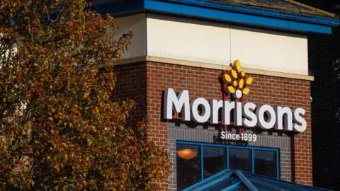 The exterior of a Morrisons on a sunny day, with the logo prominent