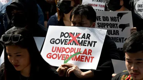 Getty Images Students, young professionals and activists of Kuki-Zo community holding placards. One of them calls the reinstated elected government an "unpopular government". 