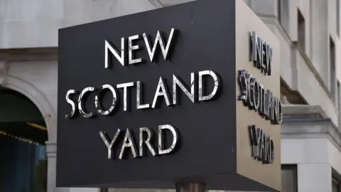 New Scotland Yard revolving sign. It is cube shaped and the lettering is in silver against a black background.