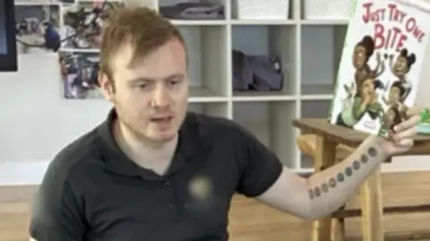 A man wearing a black shirt holding up a children's book 