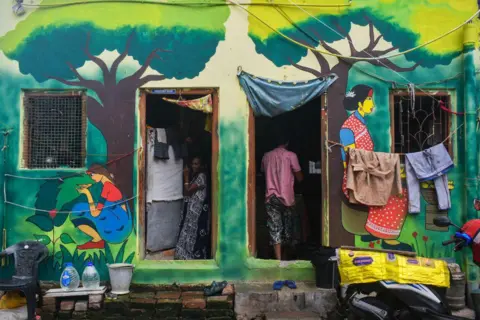 Getty Images Una mujer está parada dentro de su casa pintada de colores en una zona marginal de Calcuta, India, el 23 de junio de 2024. 