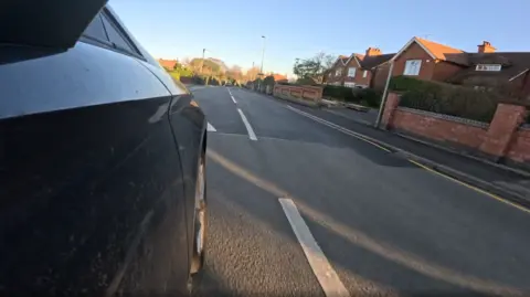 A captured image from a video filming from the wing mirror of a car, as it approaches a speed bump on Park Lane.