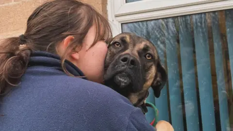 RSPCA A person in a dark blue fleece with a brown ponytail cuddles Jamie, a crossbreed dog. Jamie is looking at the camera.