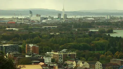 Shot of Portsmouth taken from Portsdown Hill. A mix of commercial and residential properties can be seen as well as a cruise ship and the Spinnaker Tower