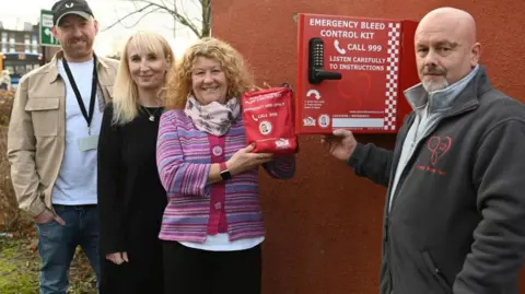 Sunderland City Council Left to right: a man in a brown jacket and jeans wearing a baseball cap, a woman with long blonde hair wearing a dark jacket and a woman with curly blonde hair in a pink and purple striped jacked all smiling. The latter is holding a red pouch. Next to her is a serious-looking man with cropped hair and a beard wearing a dark fleece. He is holding a container labelled "emergency bleed control kit"