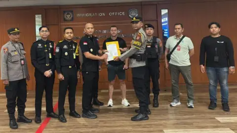 Ngurah Rai Immigration Office Steven Lyons flanked by police officers.