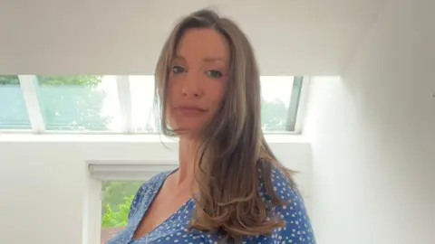 A woman with long light-brown hair wearing a blue dress with white spots.