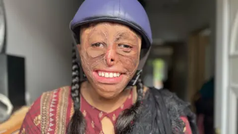 Nicola Haseler/BBC Shamiam Arif wearing her protective helmet and smiling at the camera