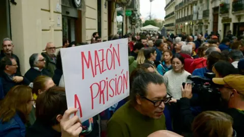 Getty Images A person holds s sign reading Mazon to prison as dozens of protesters gather outside the Valencia regional parliament