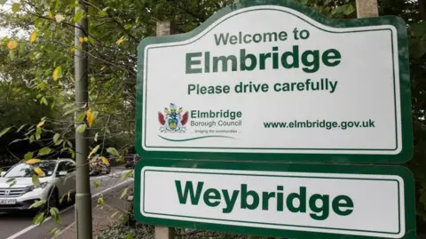 A sign for Elmbridge on the side of a road.