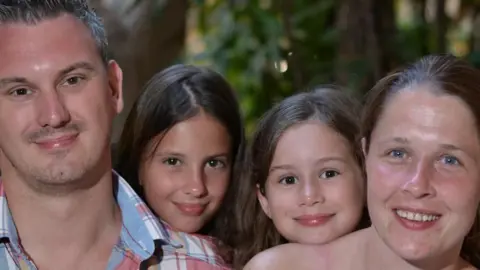 Family photograph with father, two daughters and a mum smiling on holiday.