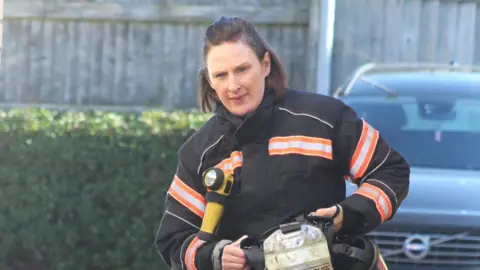 Cambridgeshire Fire and Rescue Service Ms Bourne is carrying a silver oxygen tank during a training exercise. She has a look of concentration as she walks.