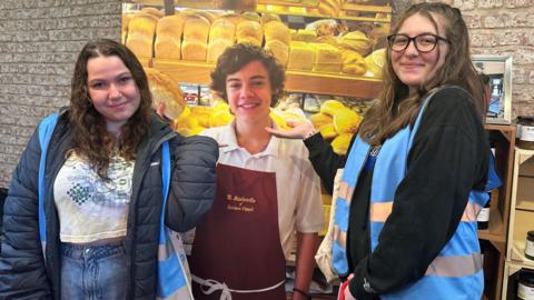 Two teenagers pose next to a picture of Harry Styles at a bakery