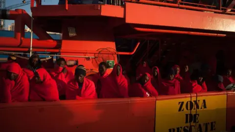 Getty Images Migrantes y refugiados cubiertos con mantas a bordo de un barco operado por el Servicio de Salvamento Marítimo de España.