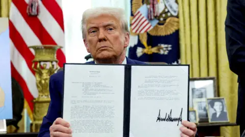 Reuters President Trump in the Oval Office holding up a declaration that he has signed. 