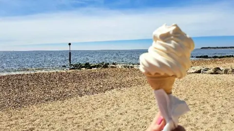 A hand holding an ice cream with the sea in the background