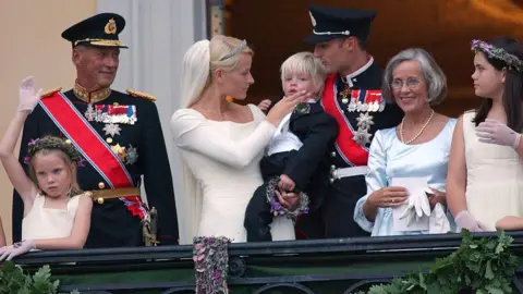 UK Press via Getty Images Several royals stand on a balcony, one in a wedding dress holding a baby