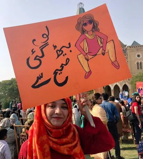 Facebook Rashida holding the "womanspreading placard"